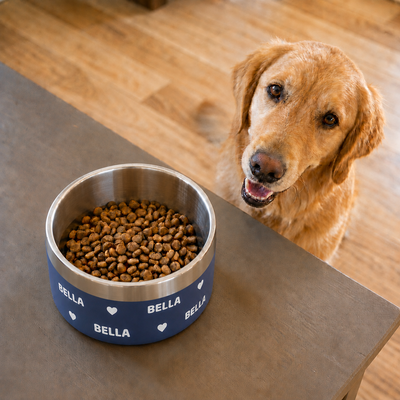 Golden retriever waiting beside a navy Personalised Wraparound Dog Bowl on a table, the name BELLA repeating around the bowl with hearts between