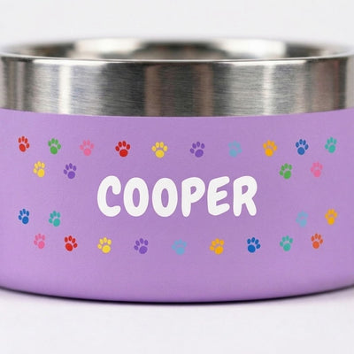 Close-up of a lilac Personalised Pattern Dog Bowl, the name COOPER surrounded by a band of multicoloured paw prints